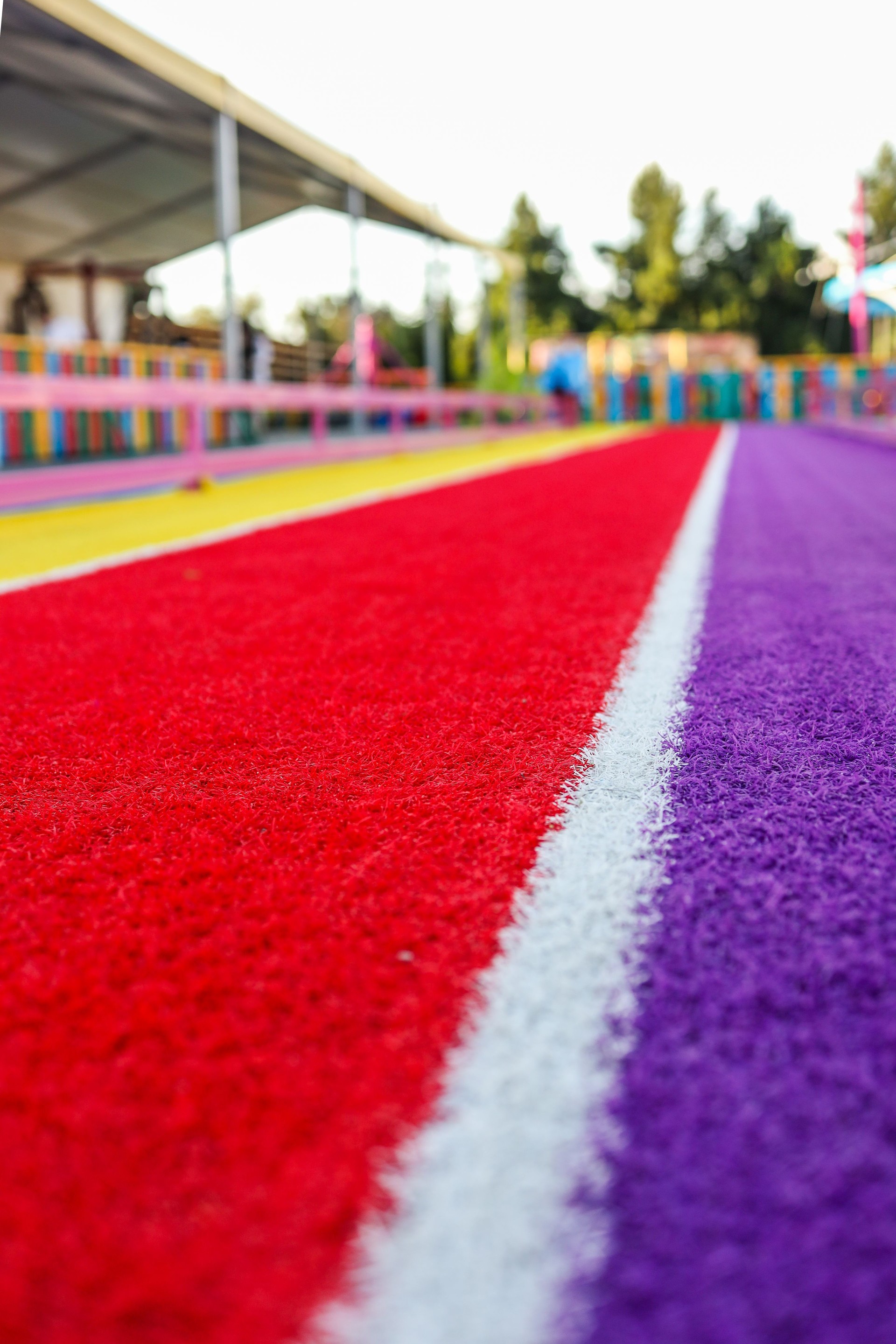 Colorful rubber running track with red, purple, yellow stripes and white line. Shot from a low angle at a children's playground or park under sunlight