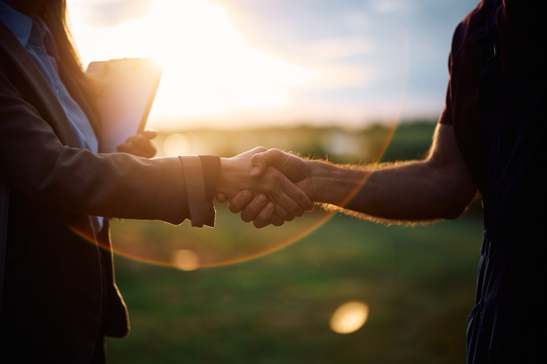 Close up of farmer handshaking with insurance agent at sunset.